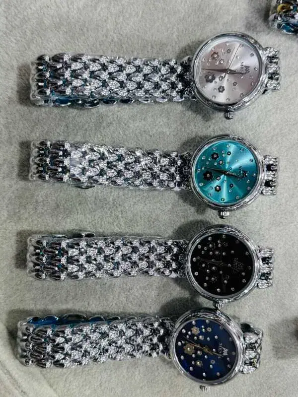 floral-themed timepiece appears to be a stylized fashion watch with a metallic link strap, featuring a dial adorned with crystals and flower motifs.